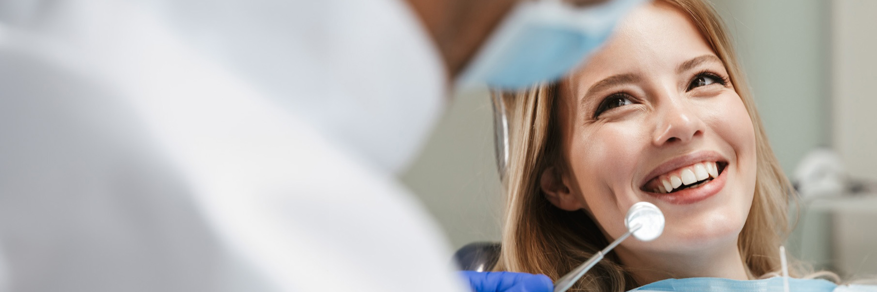 A woman smiles while seated in a dentist chair, showcasing the positive experience of dental visits